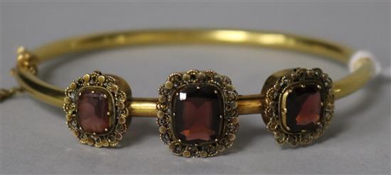 A Victorian gold and three stone garnet set hinged bangle.